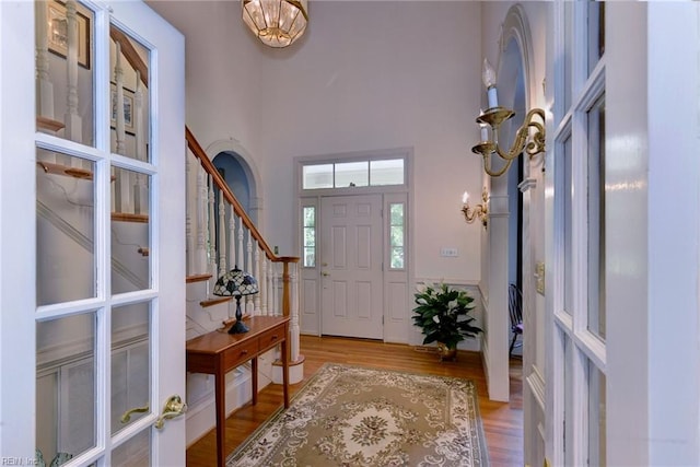 foyer entrance featuring a towering ceiling, light wood-type flooring, and an inviting chandelier