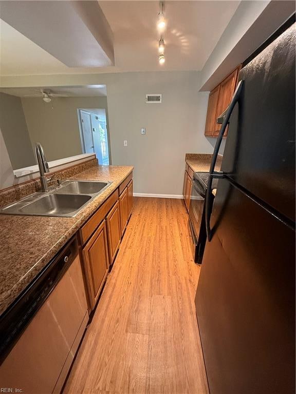 kitchen with track lighting, black fridge, stainless steel dishwasher, sink, and light hardwood / wood-style floors