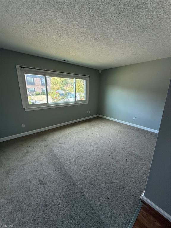 unfurnished room with a textured ceiling and dark colored carpet