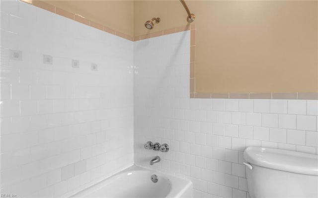 bathroom featuring toilet, tiled shower / bath, and tile walls