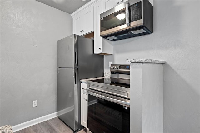 kitchen with white cabinetry, stainless steel appliances, light stone counters, and hardwood / wood-style flooring