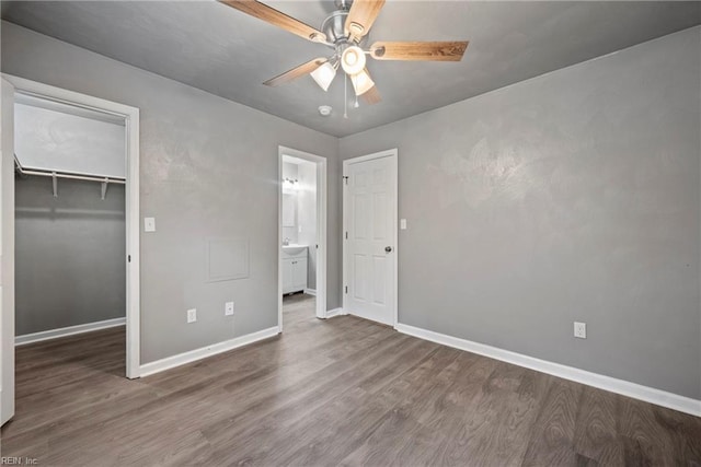 unfurnished bedroom with a spacious closet, a closet, ceiling fan, and dark wood-type flooring