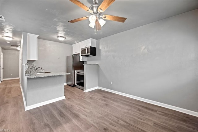 kitchen featuring sink, light stone counters, appliances with stainless steel finishes, white cabinets, and hardwood / wood-style flooring