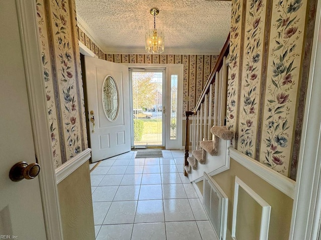 foyer featuring light tile patterned flooring, ornamental molding, a textured ceiling, and a chandelier