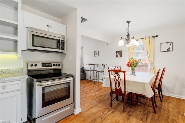 kitchen with light wood-type flooring, stainless steel appliances, pendant lighting, a notable chandelier, and white cabinets