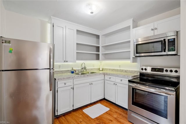 kitchen with appliances with stainless steel finishes, light wood-type flooring, light stone counters, sink, and white cabinetry