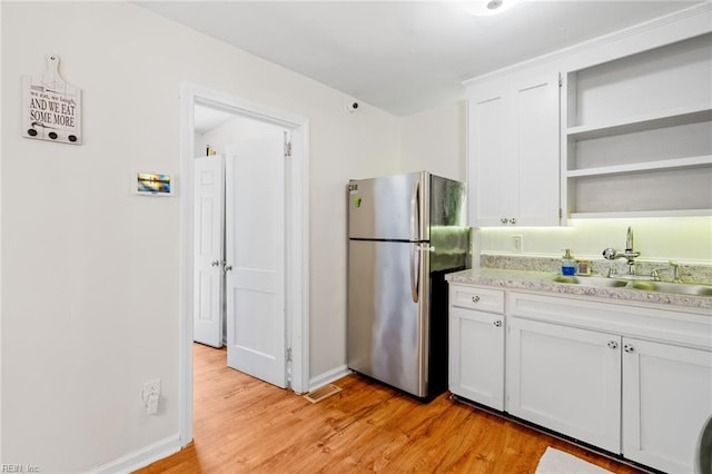 kitchen with white cabinets, light hardwood / wood-style floors, sink, and stainless steel refrigerator