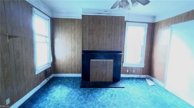 unfurnished living room with wooden walls, ceiling fan, and dark colored carpet