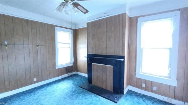 unfurnished living room featuring wooden walls, ceiling fan, and a wealth of natural light