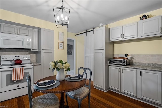 kitchen featuring a barn door, dark hardwood / wood-style flooring, backsplash, decorative light fixtures, and white appliances