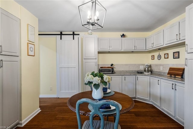 kitchen with dark hardwood / wood-style flooring, a barn door, decorative light fixtures, and light stone counters