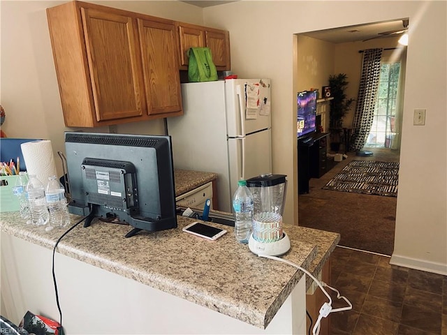 kitchen with dark colored carpet, white refrigerator, and light stone countertops