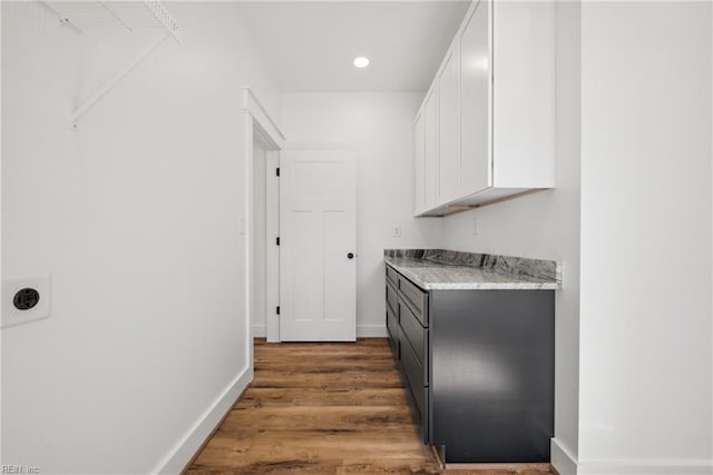 bar featuring hardwood / wood-style floors, light stone countertops, and white cabinetry