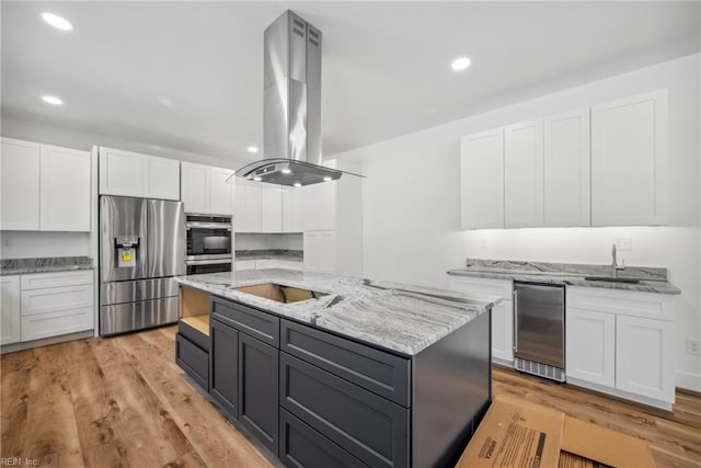 kitchen with a kitchen island with sink, white cabinets, light hardwood / wood-style floors, stainless steel appliances, and extractor fan