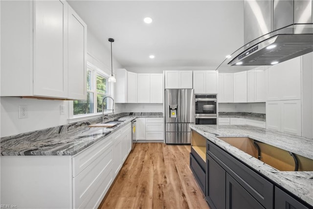 kitchen featuring white cabinets, wall chimney range hood, appliances with stainless steel finishes, light hardwood / wood-style floors, and light stone counters