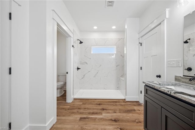 bathroom with tiled shower, hardwood / wood-style floors, vanity, and toilet