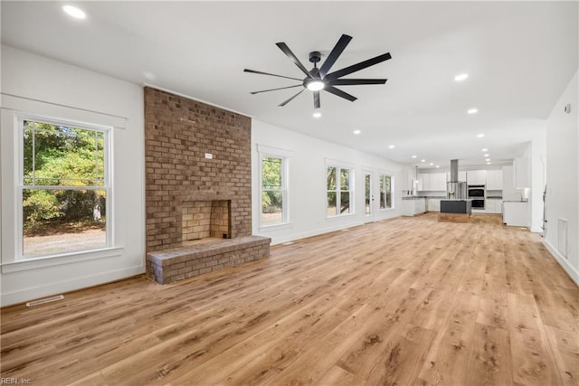 unfurnished living room featuring a fireplace, light wood-type flooring, plenty of natural light, and ceiling fan