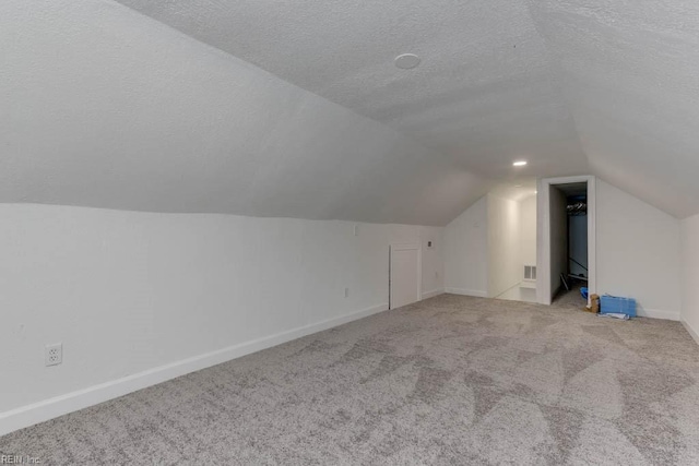 additional living space with light colored carpet, lofted ceiling, and a textured ceiling