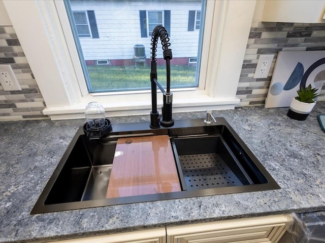 interior details with decorative backsplash, cream cabinetry, and sink