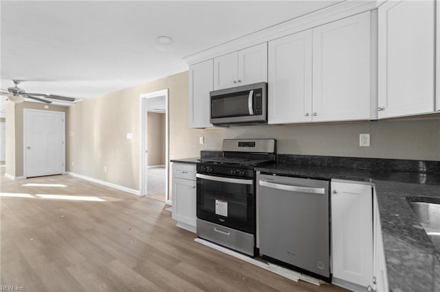 kitchen with appliances with stainless steel finishes, white cabinets, dark stone counters, ceiling fan, and light wood-type flooring