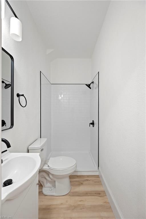 bathroom featuring toilet, wood-type flooring, and a tile shower