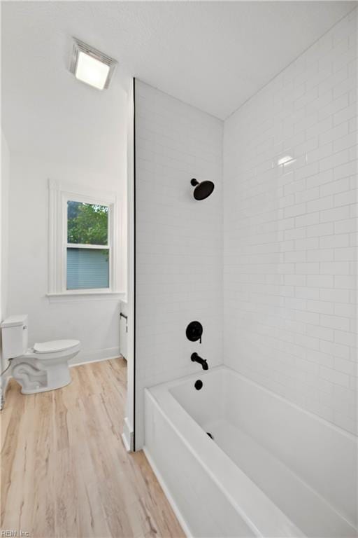 bathroom with wood-type flooring, tiled shower / bath combo, and toilet