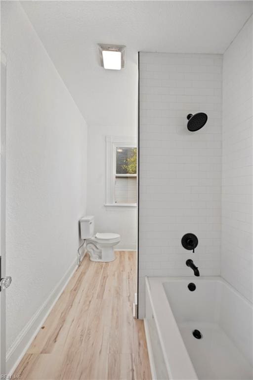 bathroom with hardwood / wood-style floors, toilet, and tiled shower / bath