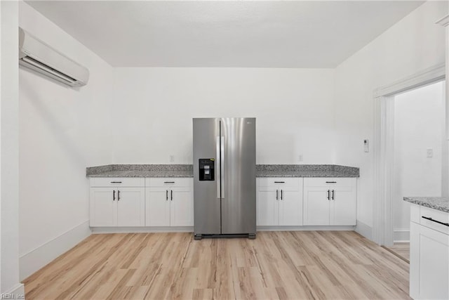 kitchen with stainless steel fridge, an AC wall unit, white cabinetry, and light hardwood / wood-style flooring