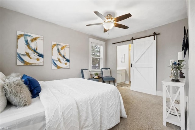 carpeted bedroom with ensuite bathroom, a barn door, and ceiling fan