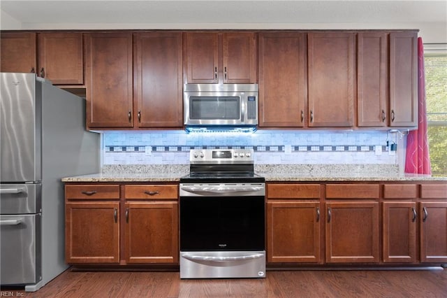 kitchen featuring backsplash, dark hardwood / wood-style flooring, light stone countertops, and stainless steel appliances