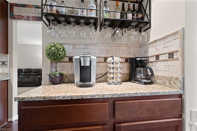 bar with decorative backsplash, light stone counters, and dark wood-type flooring