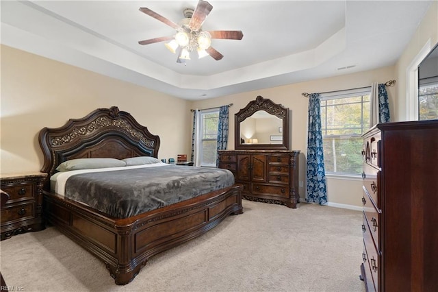 carpeted bedroom with ceiling fan, a raised ceiling, and multiple windows