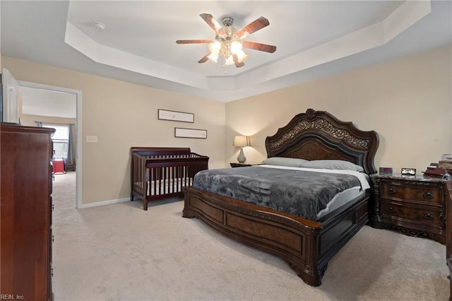 carpeted bedroom with a raised ceiling and ceiling fan