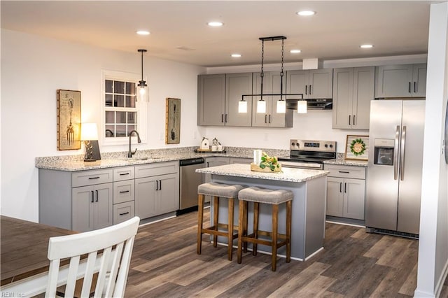 kitchen with dark wood-type flooring, decorative light fixtures, a kitchen island, light stone counters, and stainless steel appliances