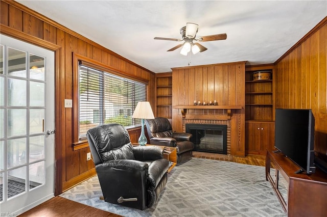 living room with ceiling fan, built in features, wood walls, a fireplace, and ornamental molding