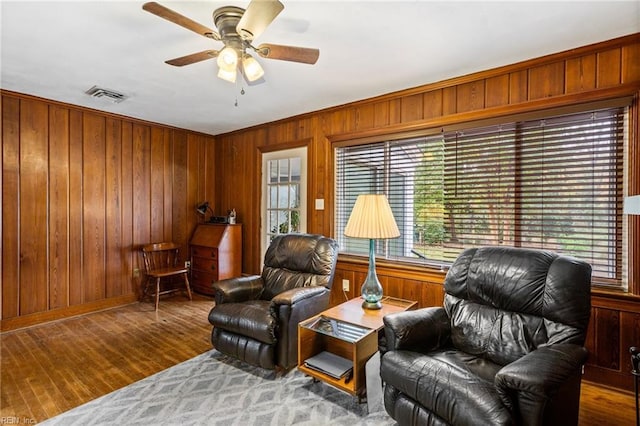 living area featuring hardwood / wood-style flooring, ceiling fan, wood walls, and crown molding