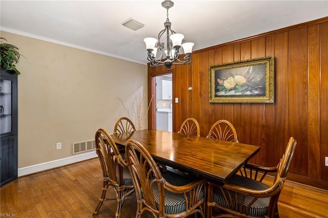 dining area with wood-type flooring, wooden walls, an inviting chandelier, and ornamental molding