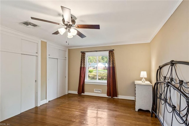 unfurnished bedroom with ceiling fan, wood-type flooring, crown molding, and two closets