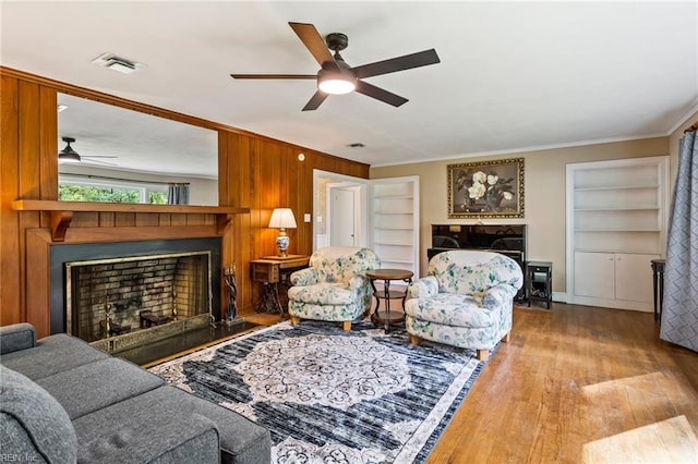 living room featuring ceiling fan, crown molding, built in features, light hardwood / wood-style floors, and wood walls