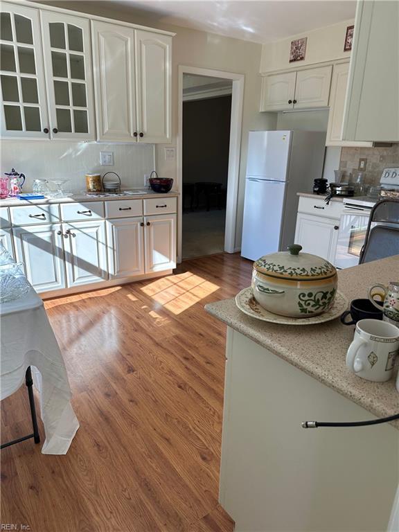 kitchen featuring decorative backsplash, white appliances, light hardwood / wood-style flooring, and white cabinetry