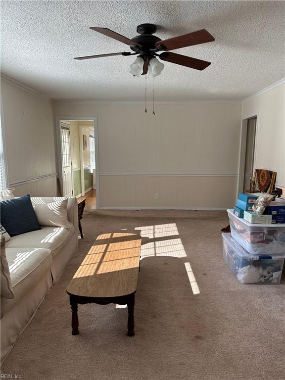 carpeted living room featuring ceiling fan, a textured ceiling, and ornamental molding