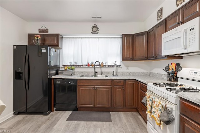 kitchen with black appliances, light stone counters, sink, and light hardwood / wood-style flooring