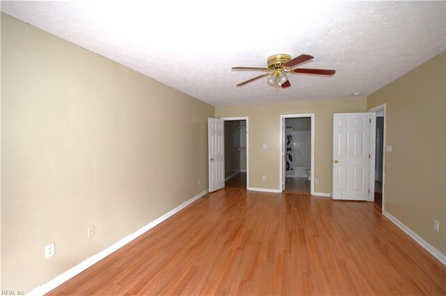 unfurnished bedroom featuring ceiling fan, a textured ceiling, a walk in closet, a closet, and light wood-type flooring