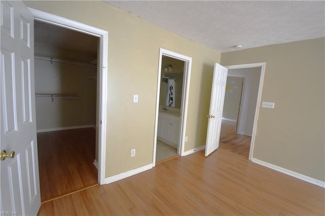 unfurnished bedroom with a walk in closet, a textured ceiling, connected bathroom, light hardwood / wood-style floors, and a closet