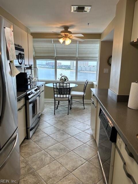 kitchen with ceiling fan, a water view, light tile patterned floors, and appliances with stainless steel finishes