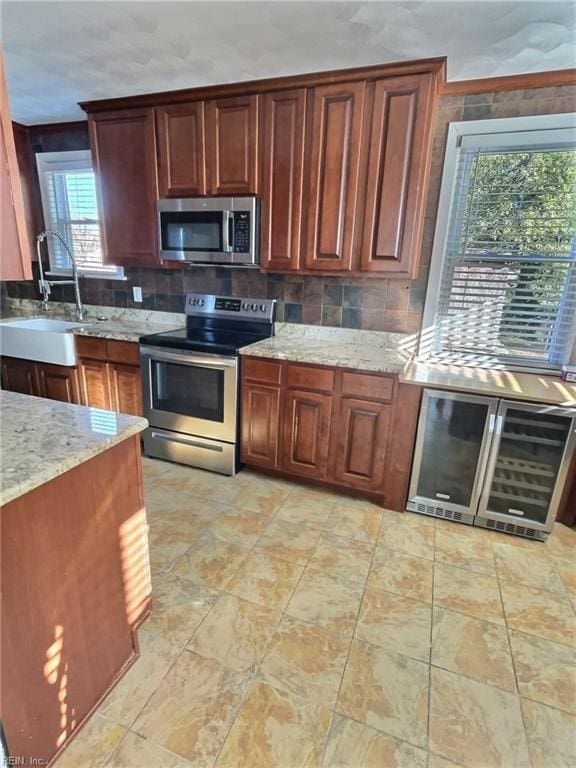 kitchen with light stone countertops, sink, tasteful backsplash, wine cooler, and appliances with stainless steel finishes