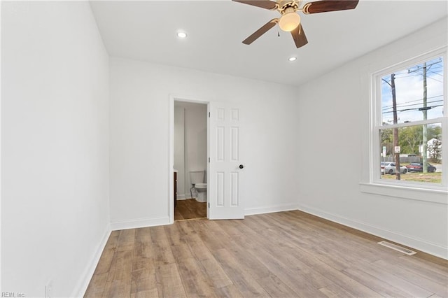 unfurnished bedroom featuring ensuite bath, light hardwood / wood-style flooring, multiple windows, and ceiling fan