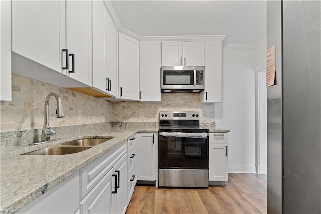 kitchen featuring appliances with stainless steel finishes, light wood-type flooring, light stone counters, crown molding, and white cabinetry