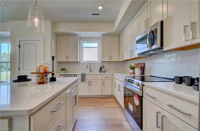 kitchen with decorative backsplash, appliances with stainless steel finishes, light hardwood / wood-style flooring, and pendant lighting