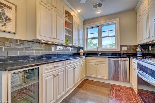 kitchen featuring decorative backsplash, stainless steel appliances, beverage cooler, sink, and light hardwood / wood-style flooring